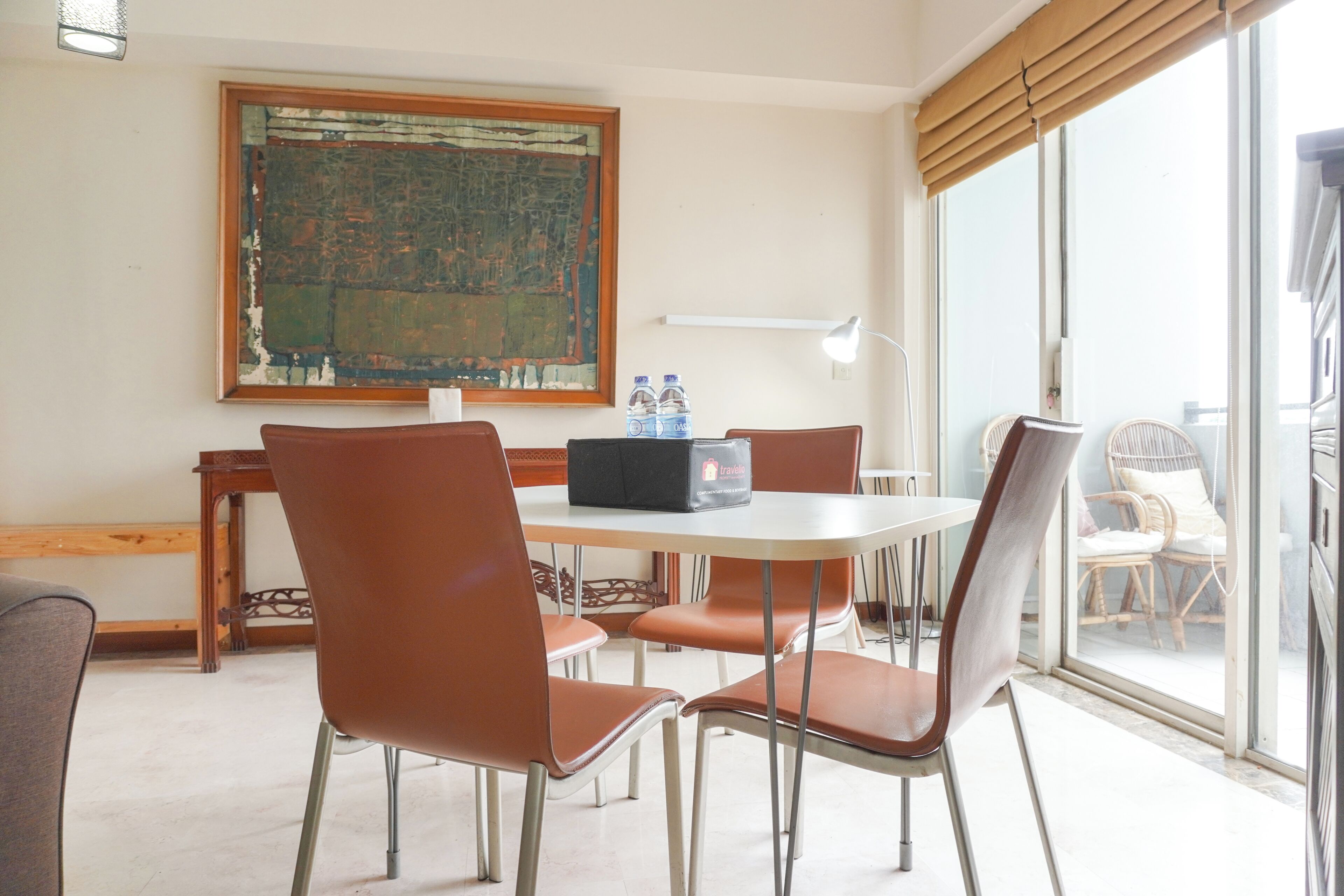 A room with a round table, brown chairs, a large abstract painting, a window with blinds, and a view of the outside.