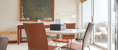 A room with a round table, brown chairs, a large abstract painting, a window with blinds, and a view of the outside.