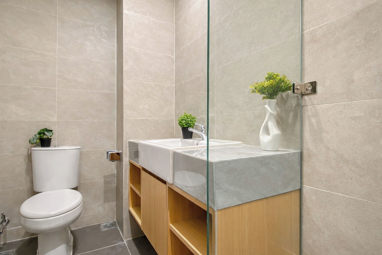 Un baño moderno con cabina de ducha de vidrio, inodoro blanco, lavamanos de mármol y estantes de madera.