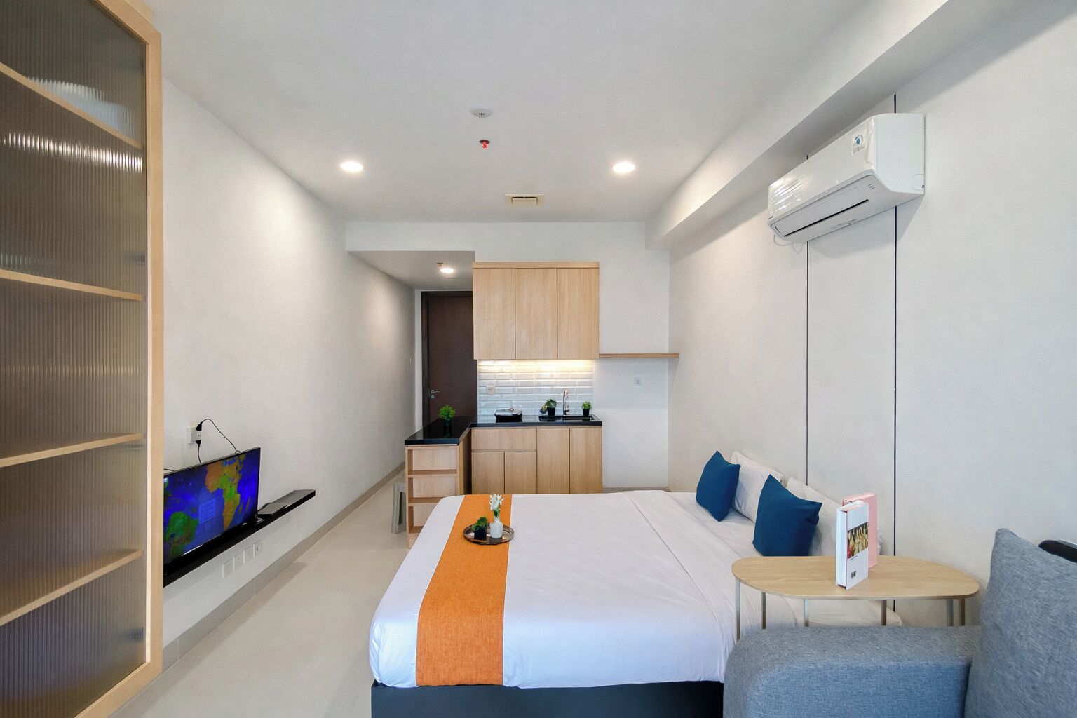 A hotel room with a bed, a TV, a small kitchen area, and a seating area.