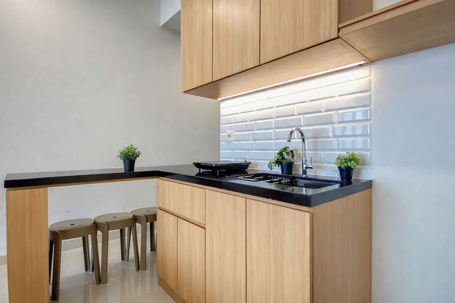 A modern kitchen with wooden cabinets, a black countertop, a stainless steel sink, and three stools.