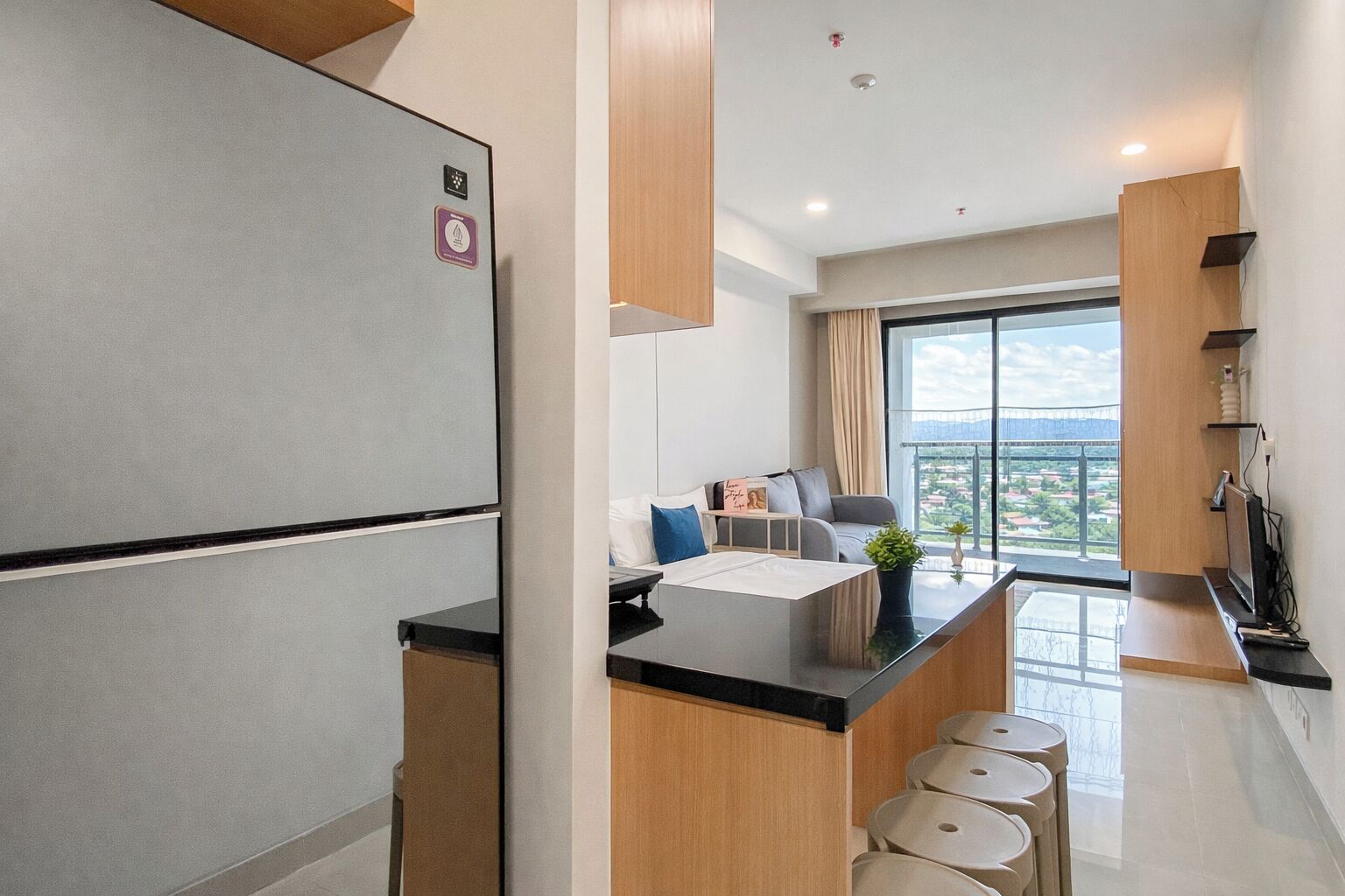 Uma cozinha moderna com geladeira, uma área de refeições com mesa e cadeiras, e vista para uma varanda com paisagem urbana.
