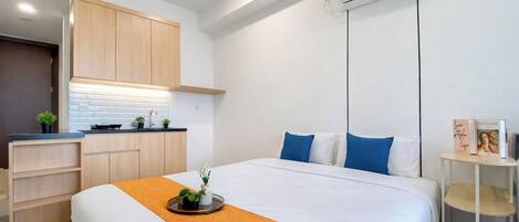 Ein modernes Hotelzimmer mit einem Bett, einer kleinen Küchenzeile und einer deckenmontierten Klimaanlage.