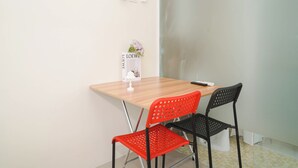 A small, modern room with a wooden table, two chairs, a vase with flowers, and a wall-mounted clock. - Nice Look Studio Apartment At Saladdin Mansion (Depok)