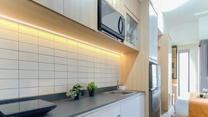 A modern kitchen with a built-in microwave, a stainless steel refrigerator, and a black sink. - Modern Japandi Studio At Sayana Bekasi Apartment (Bekasi)