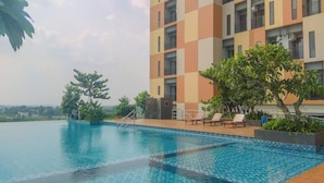 A swimming pool with tiled edges, surrounded by lounge chairs and greenery. - Modern Japandi Studio At Sayana Bekasi Apartment (Bekasi)