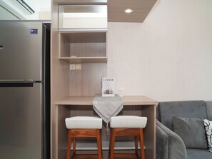 A compact kitchenette with a built-in refrigerator, a small wooden table with two stools, and a sign reading 'LODEWE.' - Good Location 1Br At Apartment Signature Park Grande (Jakarta)