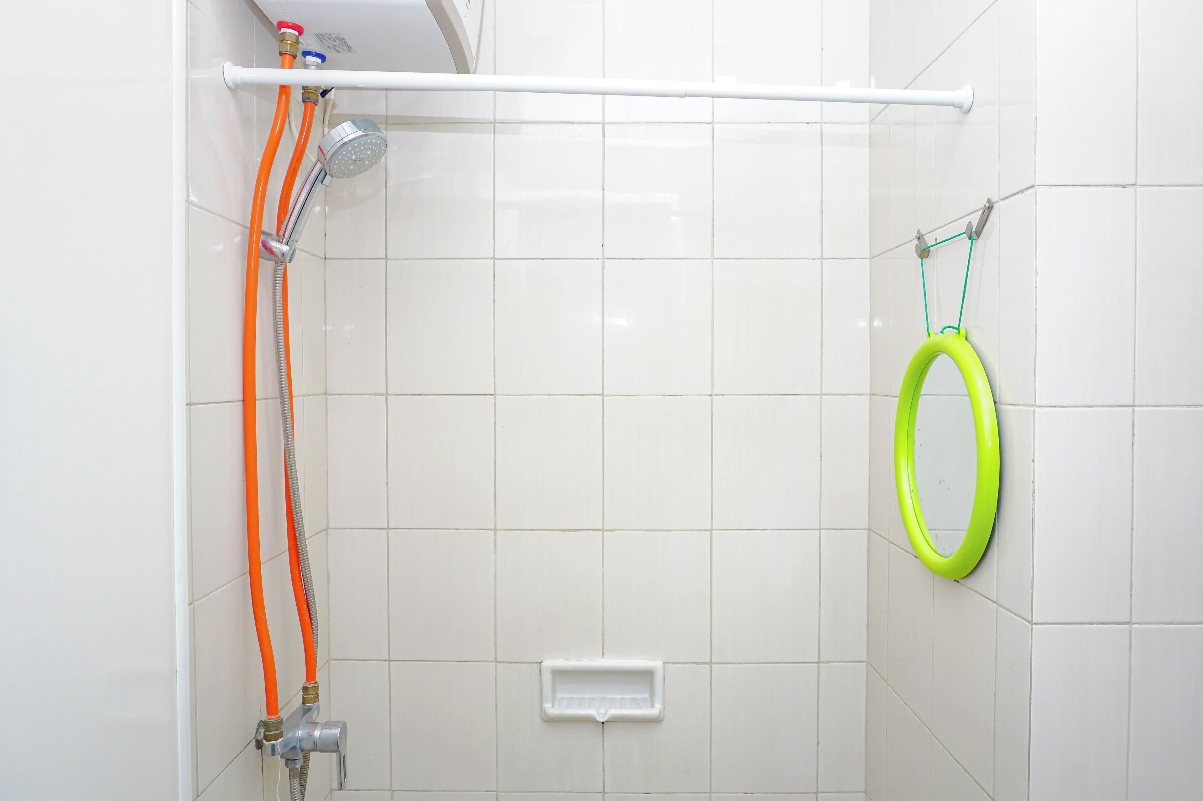 Ducha con cabezal de ducha manual y un aro de goma verde en la pared.