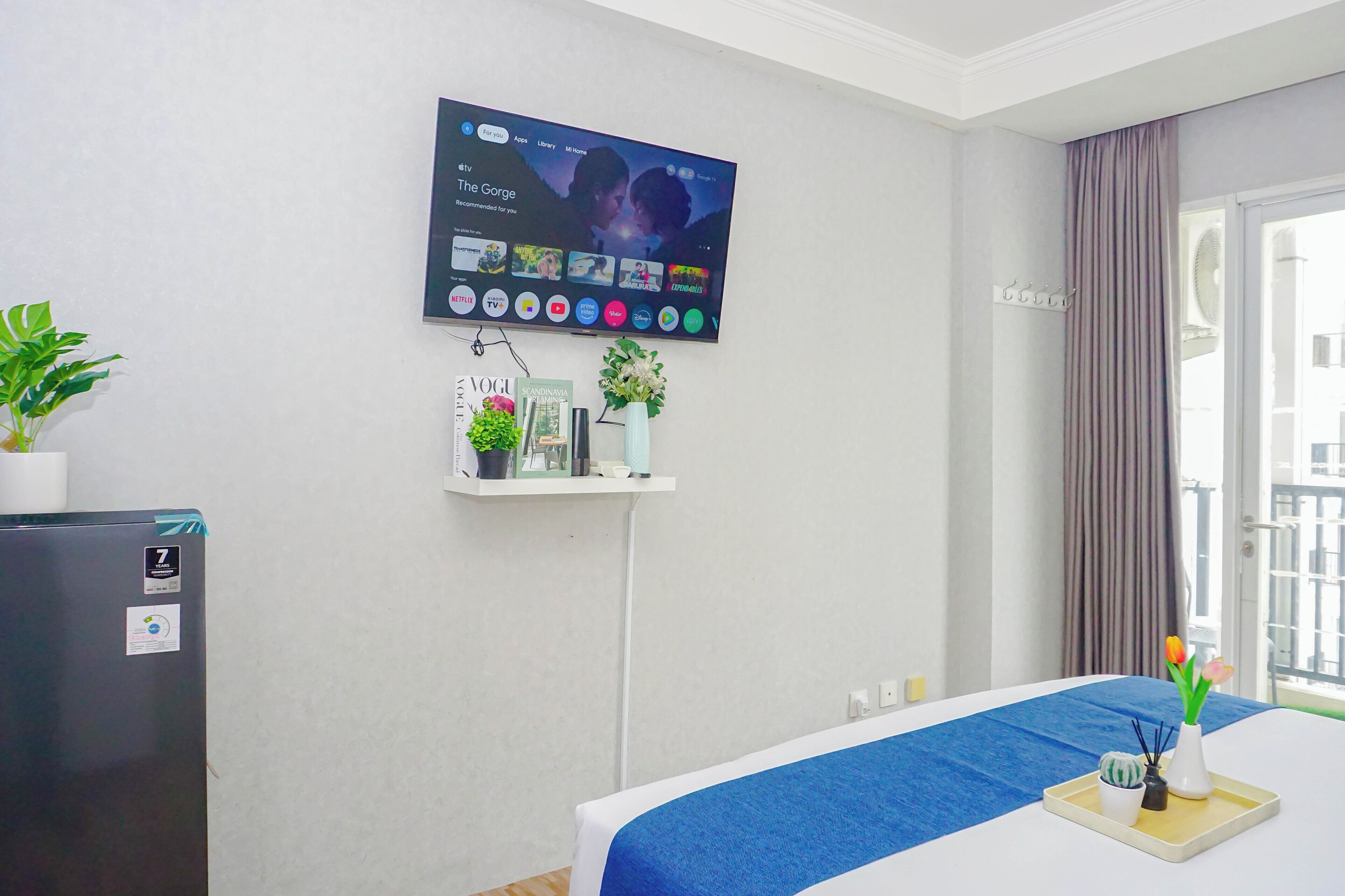 Hotelkamer met een bed, een aan de muur bevestigde televisie, een klein schapje met decoratieve objecten en een kamerplant.