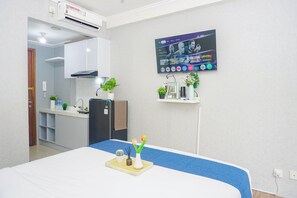 A hotel room with a bed, a TV mounted on the wall, a small kitchenette, and a bathroom visible through an open door. - Damask Style Studio At Signature Park Grande Apartment (Jakarta)