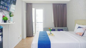 A hotel room with a bed, a TV mounted on the wall, a desk with a computer, and a window with curtains. - Damask Style Studio At Signature Park Grande Apartment (Jakarta)