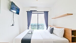Et hotelværelse med en seng, et fjernsyn hængt på væggen, et vindue med gardiner og udsigt over byen.
