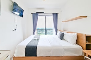 Habitación de hotel con cama, televisor montado en la pared, ventana con cortinas y vistas a la ciudad.