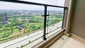 En balkon med gelænder i metal, der udover et bybillede med grønne områder og veje.
