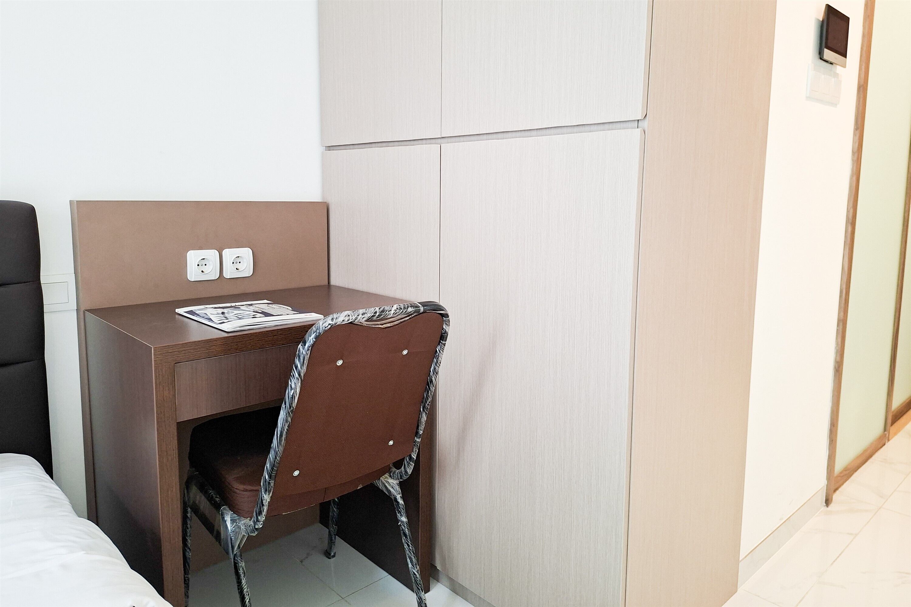 A hotel room with a wooden desk, a chair, a bed, and a wardrobe.