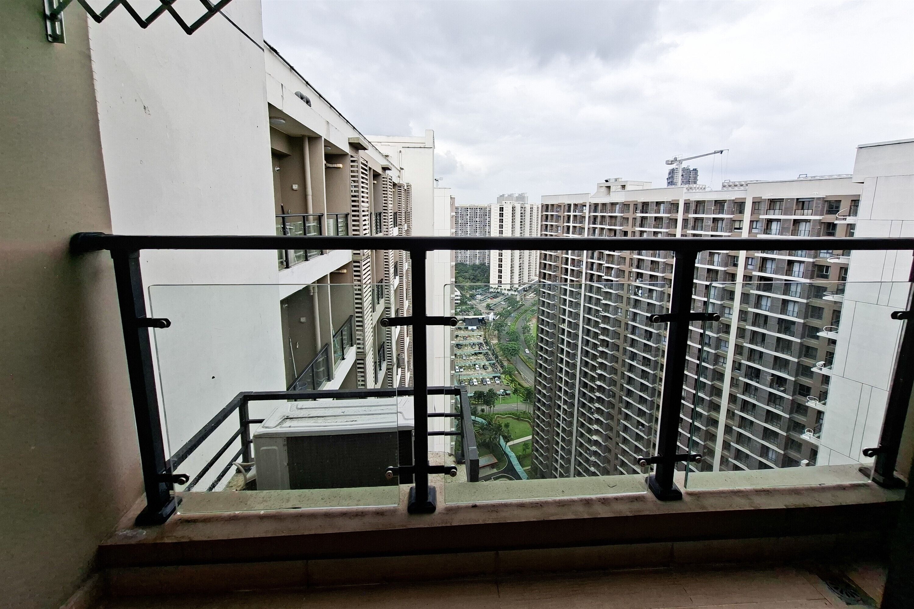 A high-rise building with a balcony railing, multiple floors, and a view of other buildings and a construction crane in the distance.