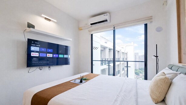 Habitación de hotel con cama, televisión integrada mostrando servicios de transmisión, ventana con vistas a edificios y unidad de aire acondicionado.