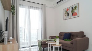 A modern living room with a sofa, a coffee table, a TV, and a balcony with curtains. - Tranquil 2Br For 4 Pax At Sky House Bsd Apartment (Pagedangan)