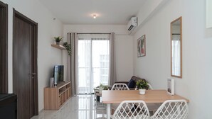 A modern living room with a wooden dining table, white chairs, a TV on a wooden stand, a sofa, and a large window with curtains. - Tranquil 2Br For 4 Pax At Sky House Bsd Apartment (Pagedangan)