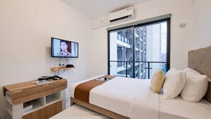 A modern hotel room with a bed, a TV, a wooden side table, and a window with a city view. - White Tone Studio For 2 Pax At Sky House Bsd Apartment (Pagedangan)