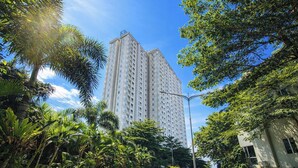 A tall residential building with multiple balconies, surrounded by lush greenery and a clear blue sky. - Compact And Warm 2Br At Apartement Skyland City Jatinangor (Hegarmanah)