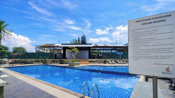 A swimming pool with a clear sky, a building with a modern design, and a signboard. - Compact And Warm 2Br At Apartement Skyland City Jatinangor (Hegarmanah)