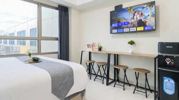 A hotel room with a bed, a TV mounted on the wall, a small table with stools, and a water dispenser. - Pleasant And Restful Studio At Apartment Springlake Summarecon Bekasi (Bekasi)