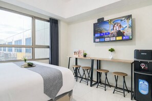 A hotel room with a bed, a TV mounted on the wall, a small table with stools, and a water dispenser. - Pleasant And Restful Studio At Apartment Springlake Summarecon Bekasi (Bekasi)