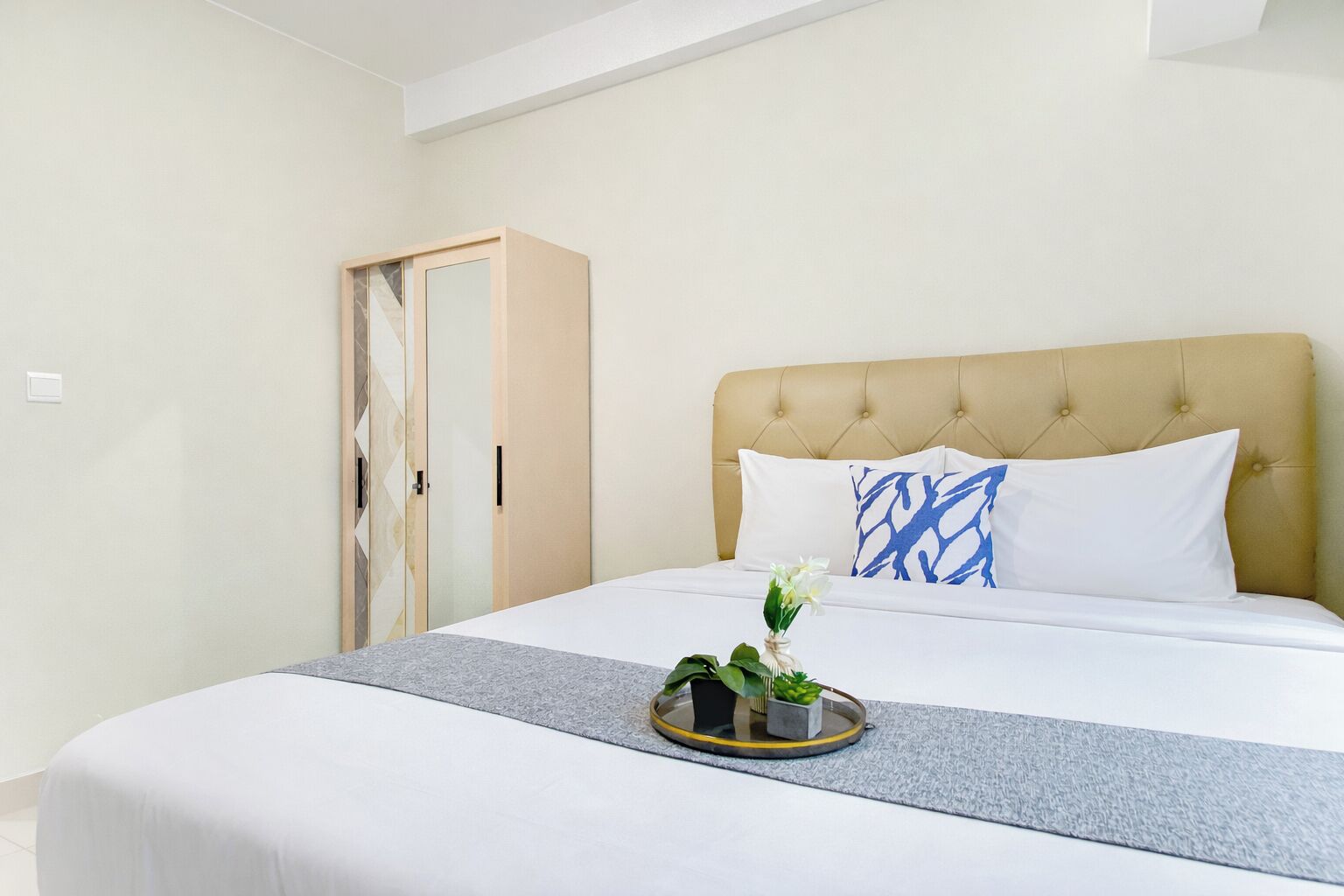 Ein Hotelzimmer mit Bett, Nachttisch mit Pflanze, Kleiderschrank und Kopfteil mit Kissen.