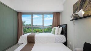 A hotel room with two beds, a large window, a view of greenery, and a mounted lamp. - Chic And Cozy Studio Space At Apartment Springlake Summarecon Bekasi (Bekasi)
