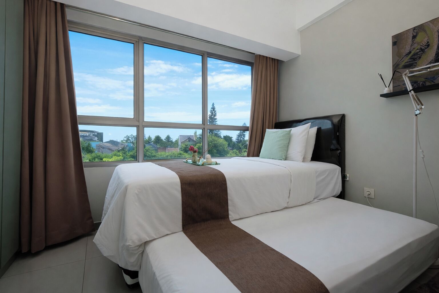 Een hotelkamer met een bed, een raam met gordijnen, een schilderij aan de muur en uitzicht op groen.
