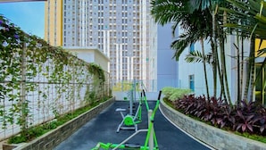An outdoor gym area with exercise equipment, surrounded by a low stone wall and greenery. - Chic And Cozy Studio Space At Apartment Springlake Summarecon Bekasi (Bekasi)