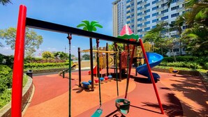 A playground with swings, a slide, and a climbing structure. - Chic And Cozy Studio Space At Apartment Springlake Summarecon Bekasi (Bekasi)