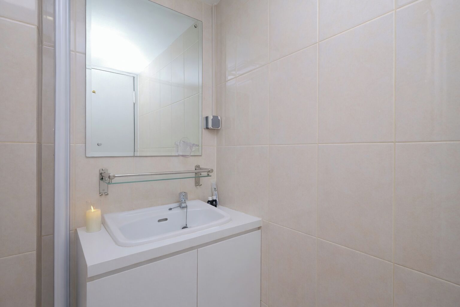 Un baño con un lavabo blanco, un estante de cristal, un espejo y un secador de manos.