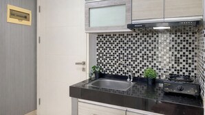 Une cuisine avec un plan de travail noir, un évier en acier inoxydable et une cuisinière. Le mur derrière l’évier est recouvert de carreaux, et il y a un meuble avec une porte en verre.