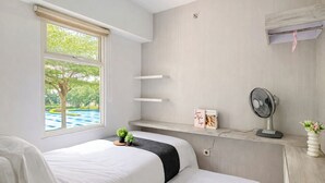 Une chambre avec deux lits, une fenêtre donnant sur une piscine, un ventilateur et une étagère avec des livres et un vase.