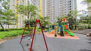Un terrain de jeux avec des balançoires et un toboggan, entouré de verdure et de grands immeubles.