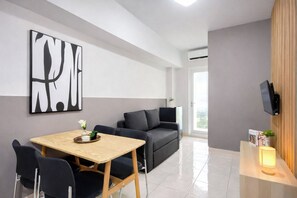 A modern living room with a sofa, a dining table with chairs, a TV mounted on the wall, and a large abstract painting. - Fully Furnished 2Br Apartment At Springlake Summarecon Bekasi (Bekasi)
