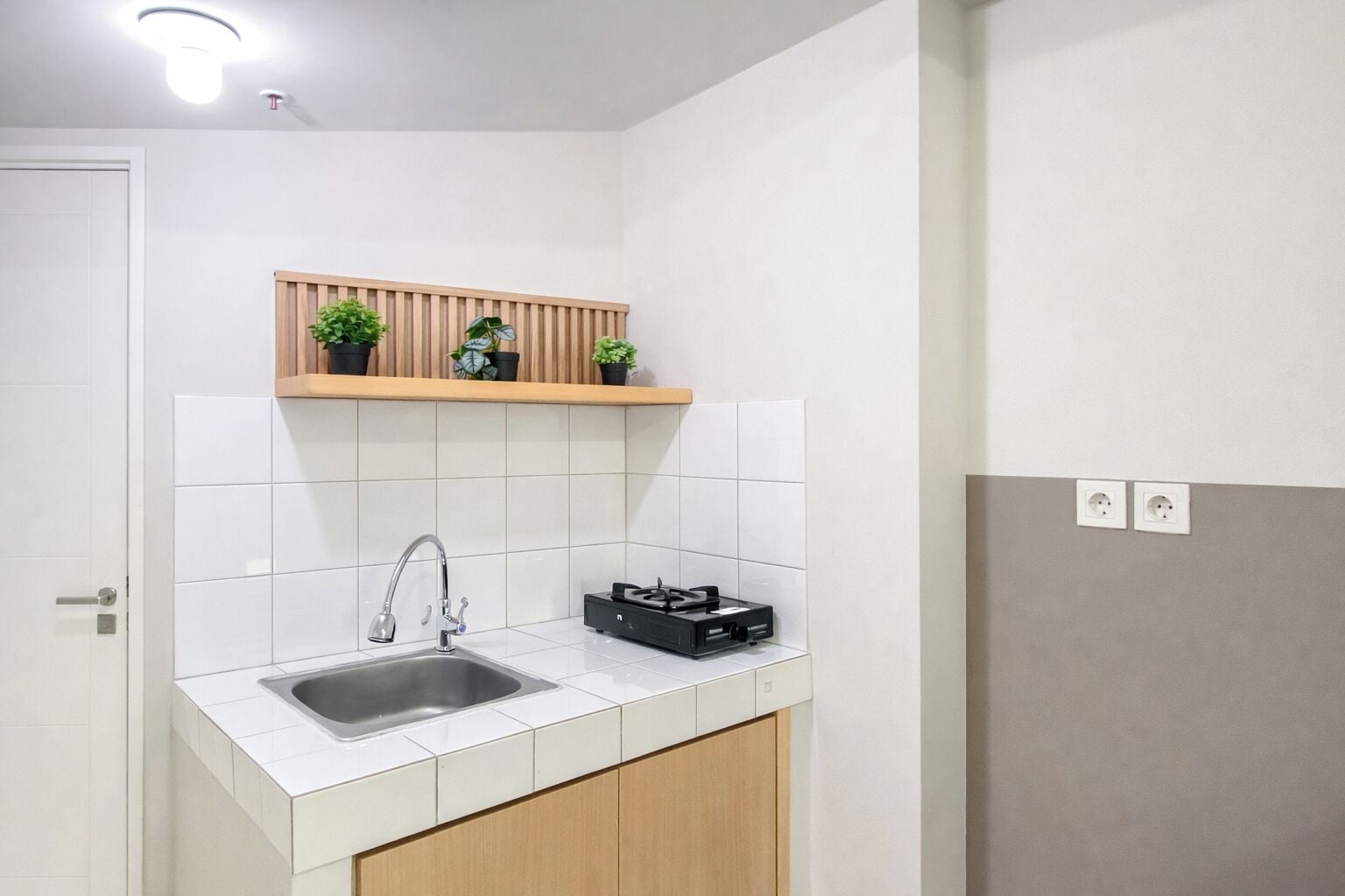 A small kitchenette with a sink, a wooden shelf with potted plants, and a gas stove.