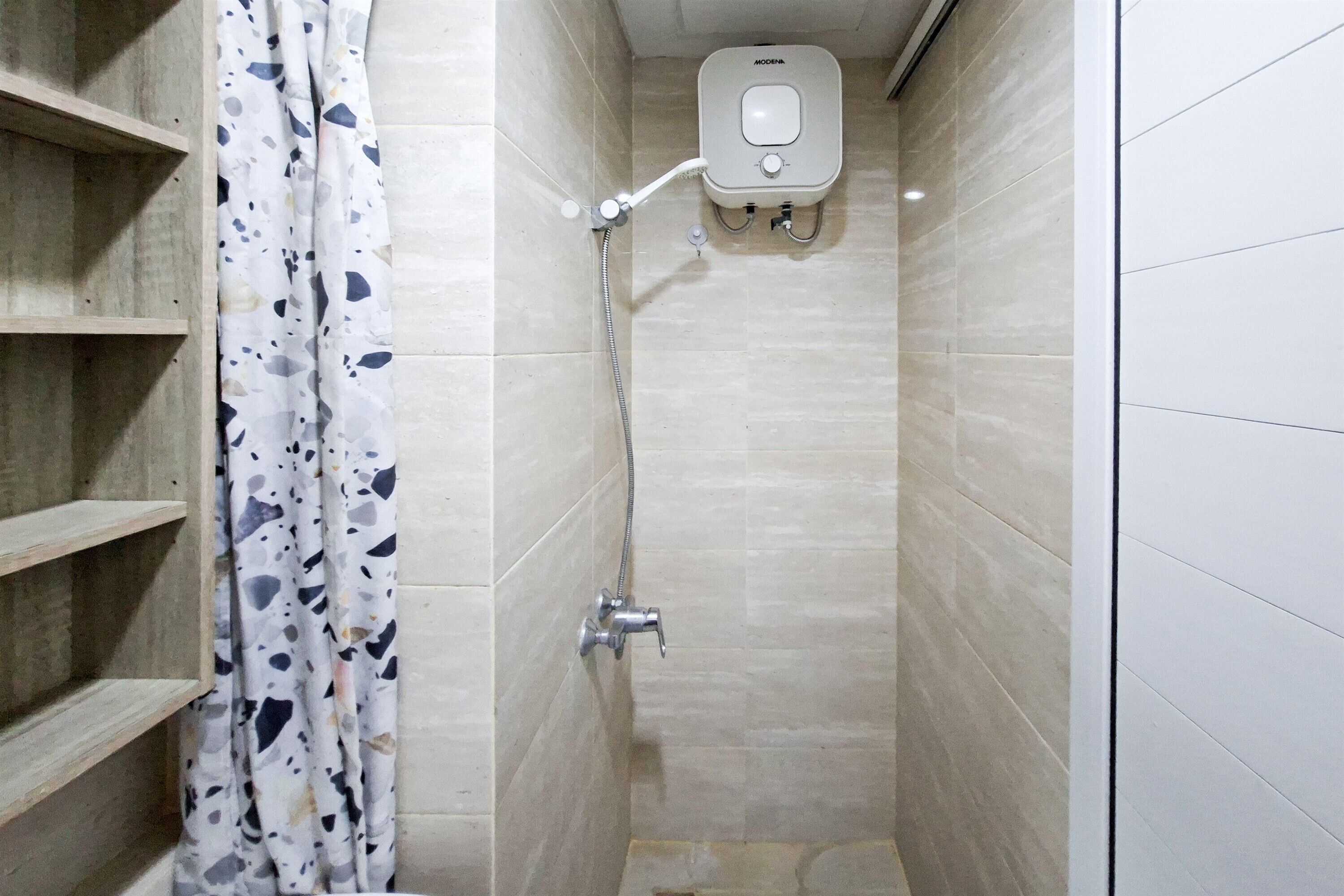 A shower with a handheld showerhead, a wall-mounted control panel, and a shower curtain with a speckled pattern.