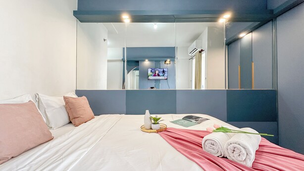 A modern hotel room with a large bed, a flat-screen TV, a mirror, and a small plant on the bedside table. - Restful Blue Studio At Suncity Residence (Sidoarjo)