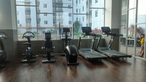 A gym with exercise equipment, large windows, and a view of a residential building. - Restful Blue Studio At Suncity Residence (Sidoarjo)