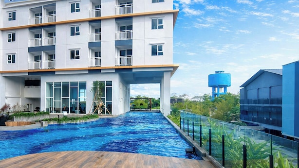 A modern hotel with a swimming pool, a wooden deck, and a view of the surrounding greenery. - Lavish 2Br Without Kitchen At Suncity Residence (Sidoarjo)