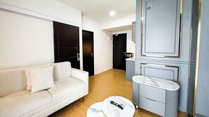 A modern living room with a white sofa, a marble coffee table, and a grey cabinet with a mirror. - Lavish 2Br Without Kitchen At Suncity Residence (Sidoarjo)