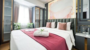 A hotel room with a large bed, a bedside table, a wardrobe, and a large abstract painting on the wall. - Lavish 2Br Without Kitchen At Suncity Residence (Sidoarjo)