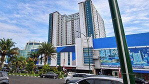 A high-rise building with multiple floors, a blue storefront with a KFC sign, and palm trees in the foreground. - Lavish 2Br Without Kitchen At Suncity Residence (Sidoarjo)