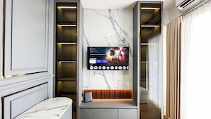 A modern living room with a marble wall, a TV mounted above a seating area, and a built-in shelving unit. - Lavish 2Br Without Kitchen At Suncity Residence (Sidoarjo)
