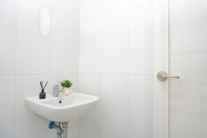 Un bagno con un lavandino bianco, una pianta in vaso e una porta con maniglia.