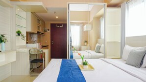 A hotel room with a bed, a desk, a chair, a small kitchen area, and a bathroom visible through an open door. - Comfortable And Pleasant Studio At Apartment Tamansari Mahogany Karawang (Karawang)