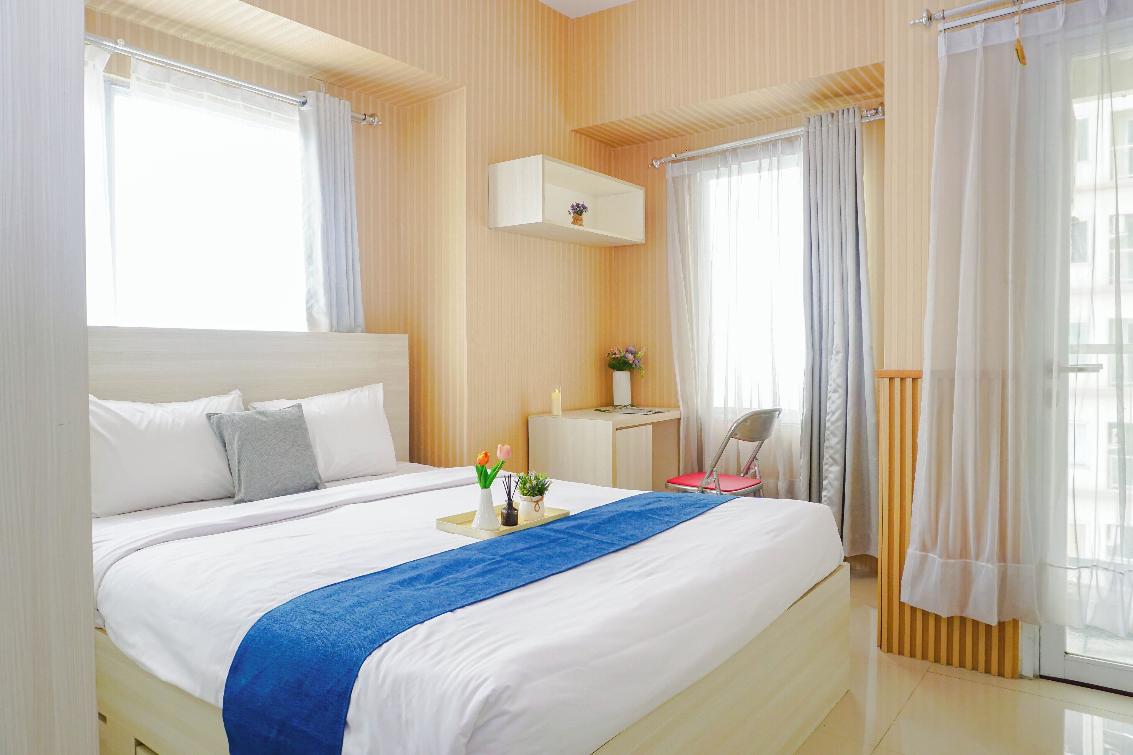 A hotel room with a large bed, a small desk, a chair, and a window with curtains.